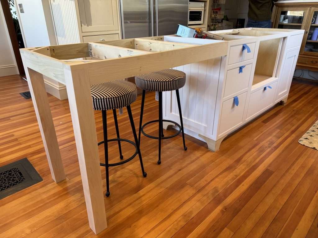 Custom kitchen island designed by Cedars & Birch Kitchens, with beaded-panel doors, drawers, and a maple seating overhang, shown during installation