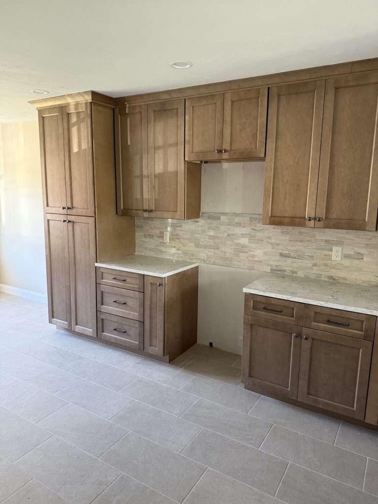 Stained shaker-style kitchen cabinets with quartz countertops and a tile backsplash in a spec house